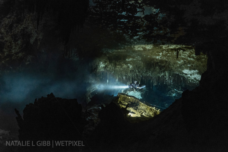 Glenn Farquhar's strong primary light punches into the darkness, illuminating sediment in the water and giving a sense of depth to this photo from Cenote Minotauro. 