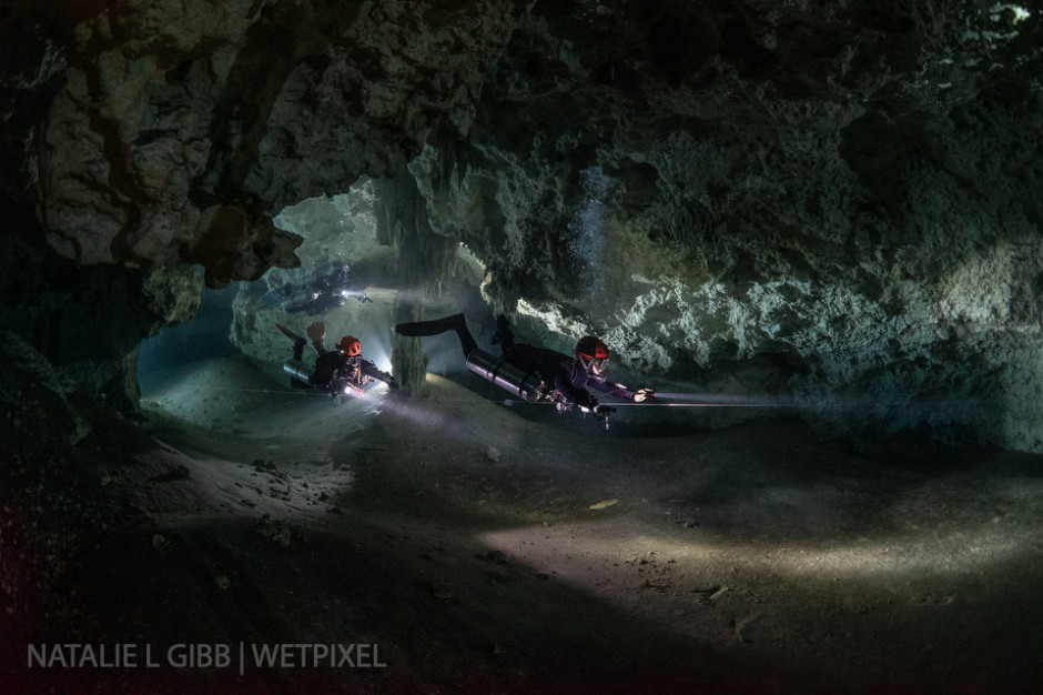 Divers Nick, Nik, and Troy turn a corner at Cenote Nohoch Nah Chich. Each divers holds his own video light to illuminate his face. 