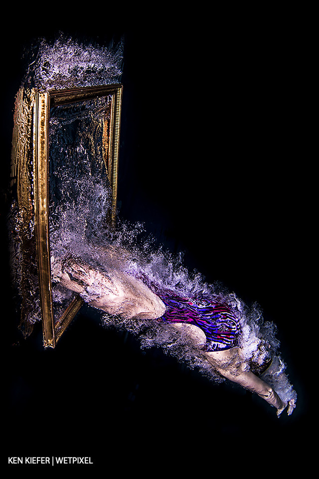 Diving through a frame on the surface of the water with a black backdrop.