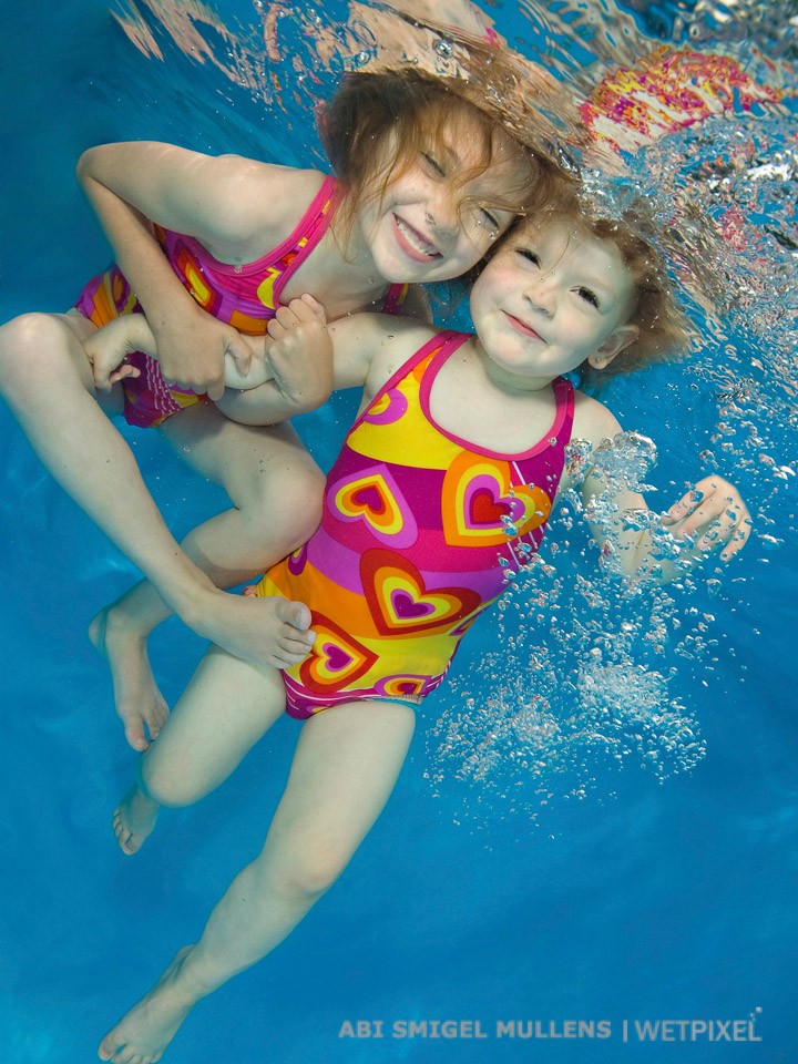 Adorable sisters heart to heart underwater.