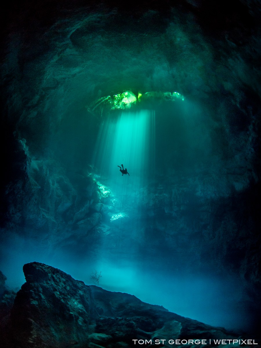 A solo diver ascending in the sunbeams at the majestic Cenote El Pit